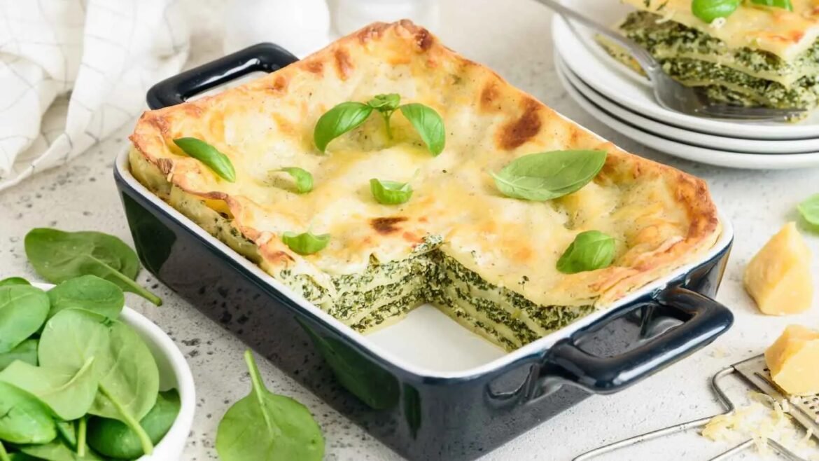 Baked spinach lasagna in a blue casserole dish with melted cheese and basil garnish on top
