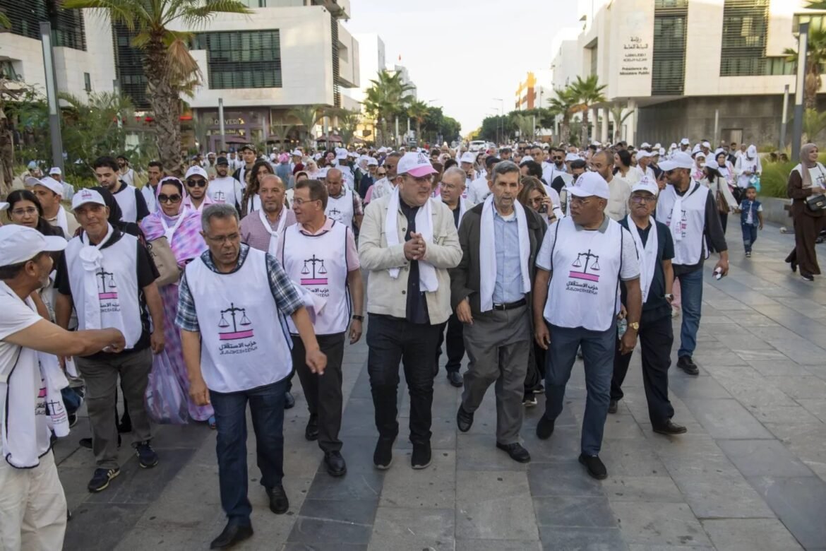 Group of people walking together in a city plaza, many wearing white vests with a scales emblem, outlining a peaceful march in a modern street.