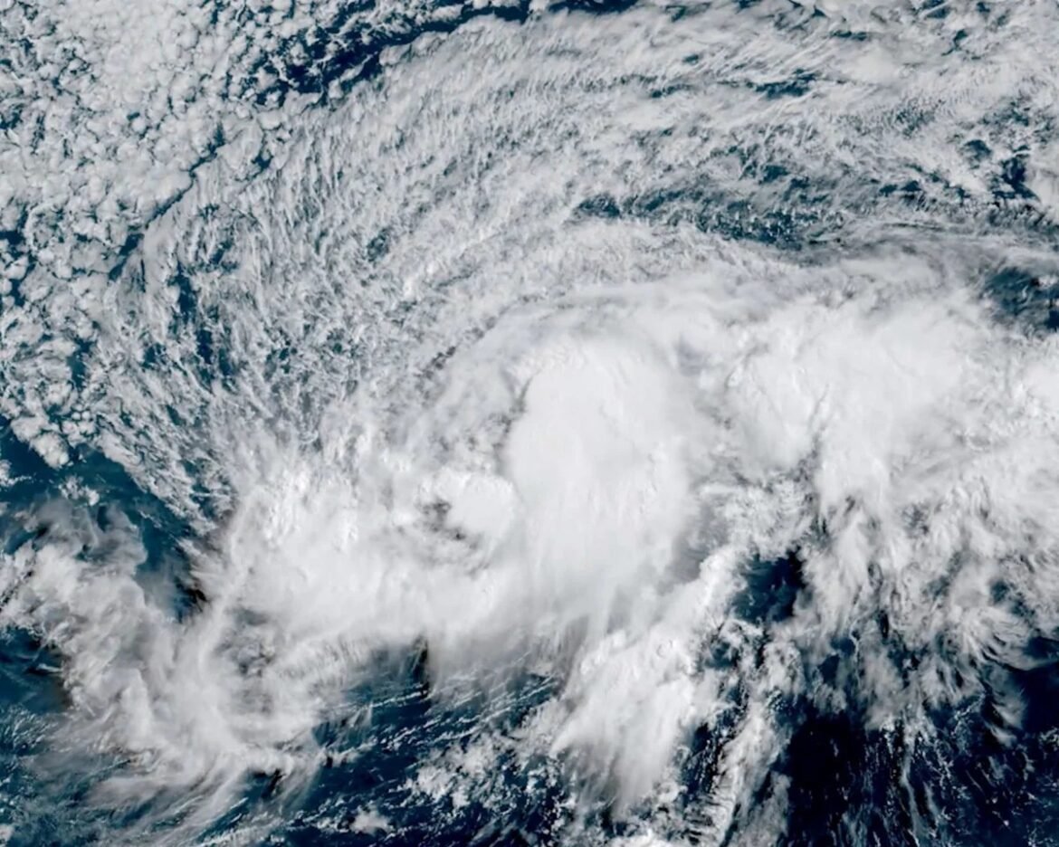 Satellite view of a tropical cyclone forming over the ocean with a dense circular cloud mass and spiral bands around a central eye area.
