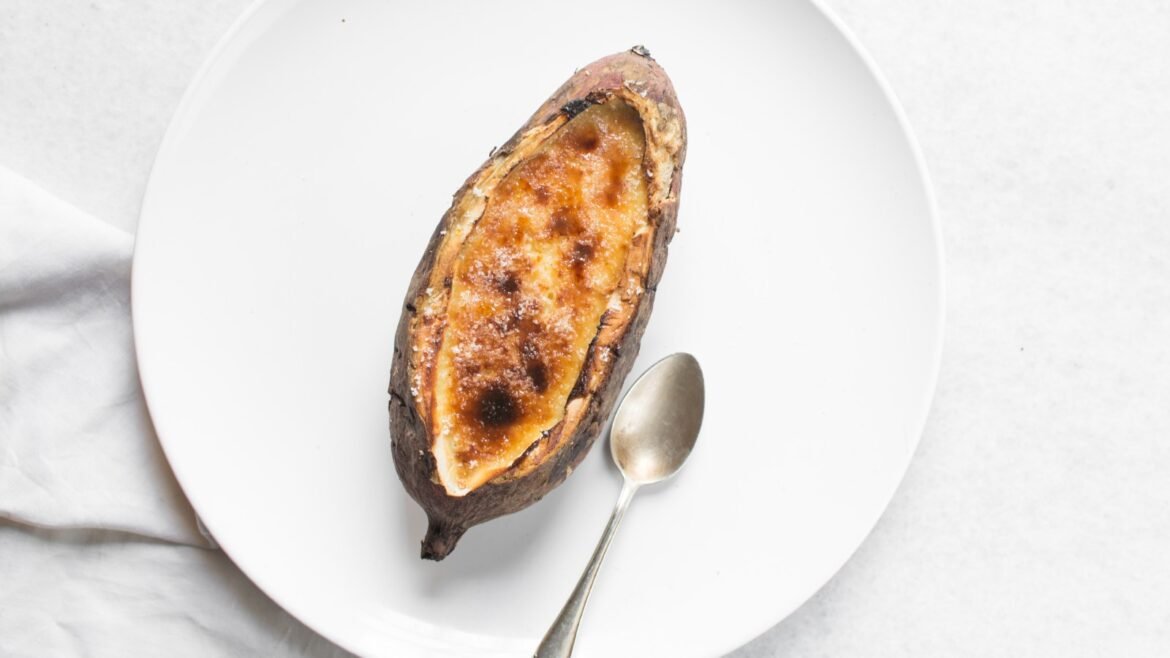 Baked sweet potato on a white plate with a spoon beside it.