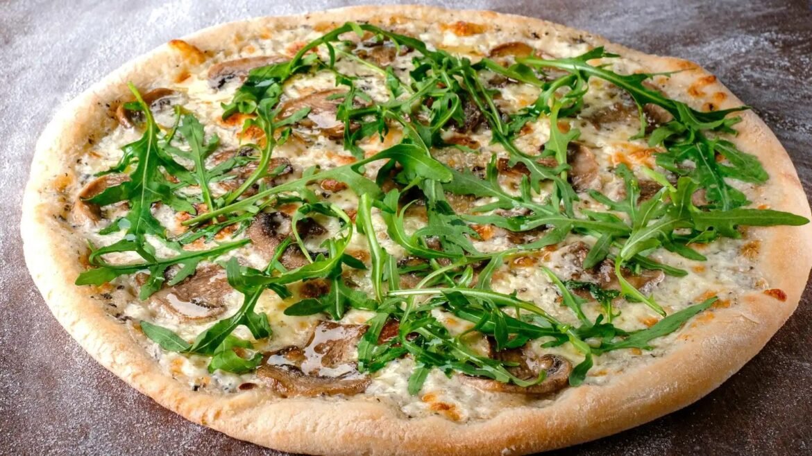 Pizza topped with fresh arugula, mushrooms, and melted cheese on a golden crust.