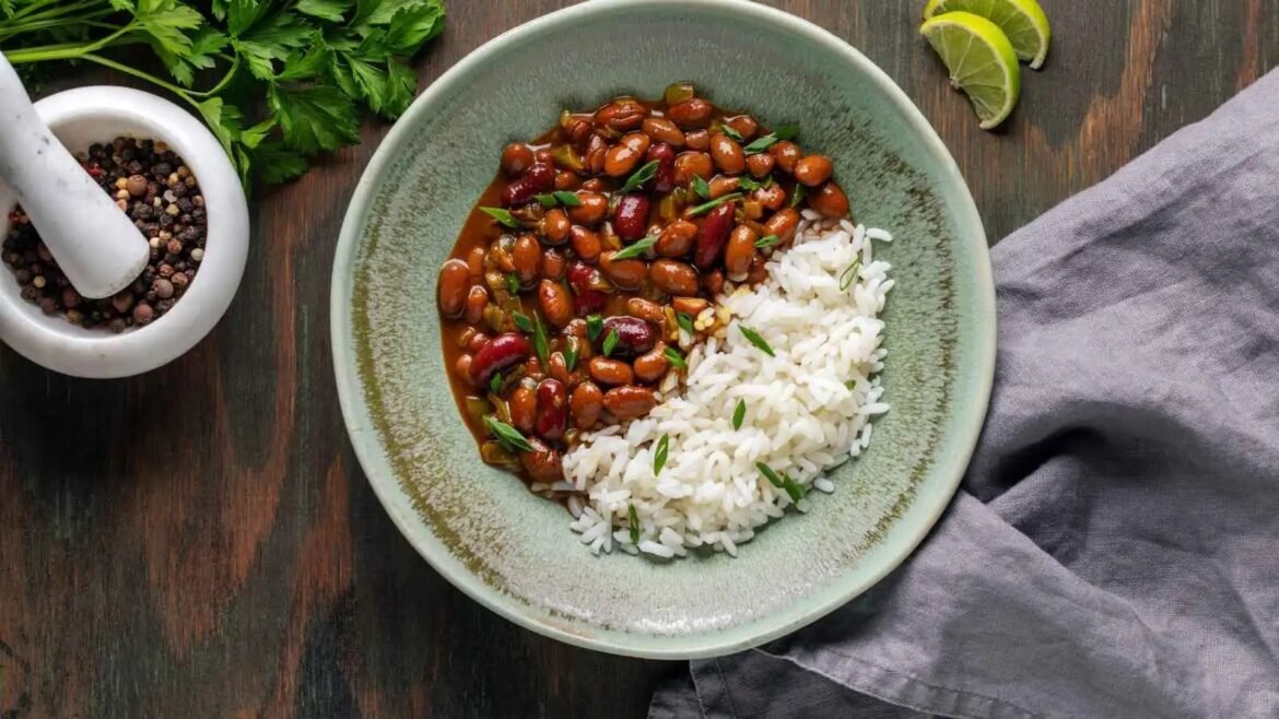 Plate of white rice with brown beans in sauce, garnished with herbs on a green ceramic plate, on a dark wooden table with lime wedges nearby.