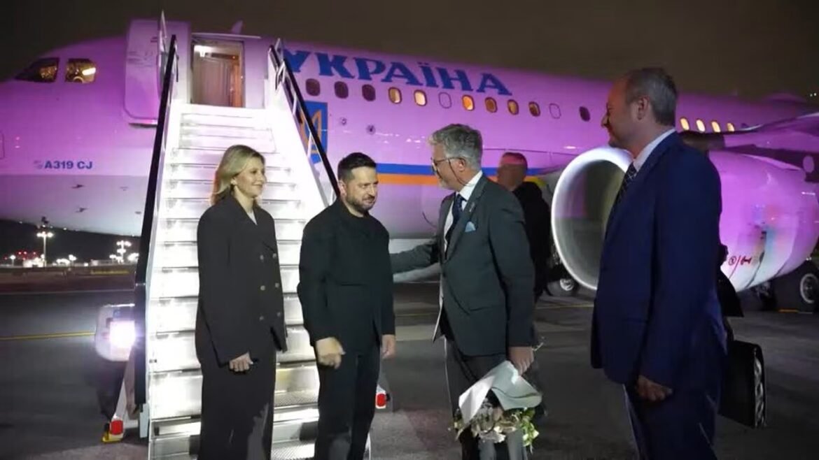 Group of four people in formal attire greet each other on an airport tarmac beside a Ukraine International Airlines plane at night with stairs leading to the door.