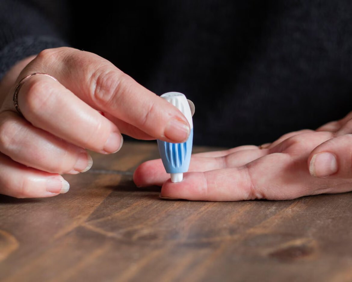 Person applies a small lancet to their fingertip to draw a blood sample on a wooden table