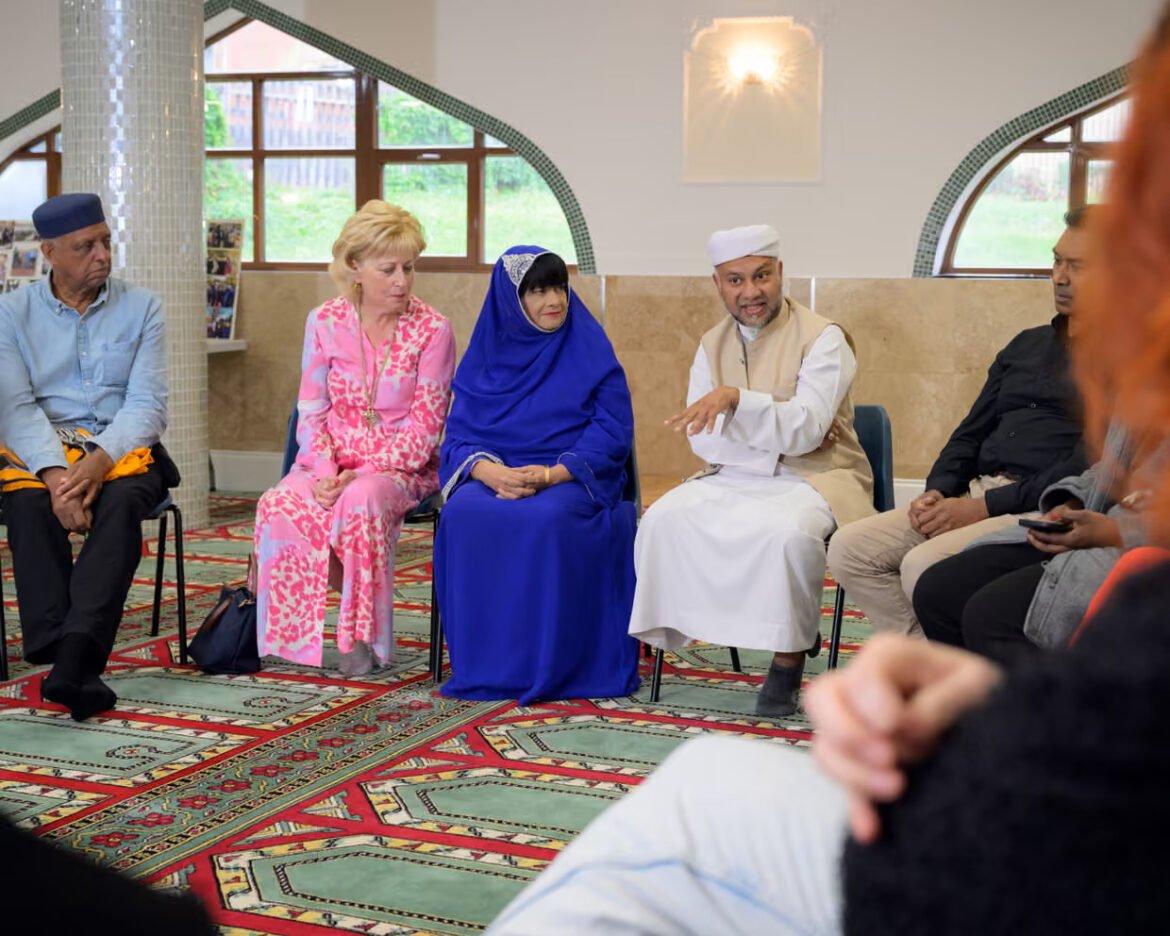 People sit in a circle in a bright room, engaged in conversation during a group discussion, wearing colorful traditional clothing and head coverings.