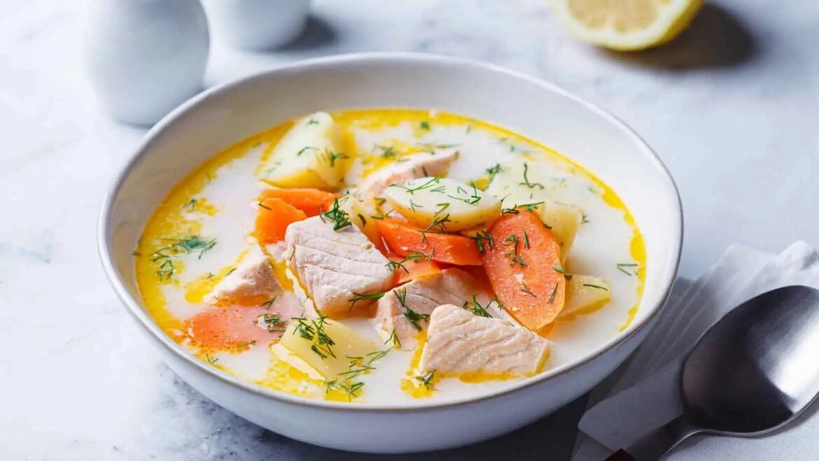 Creamy chicken and potato soup with carrots, garnished with dill in a white bowl.