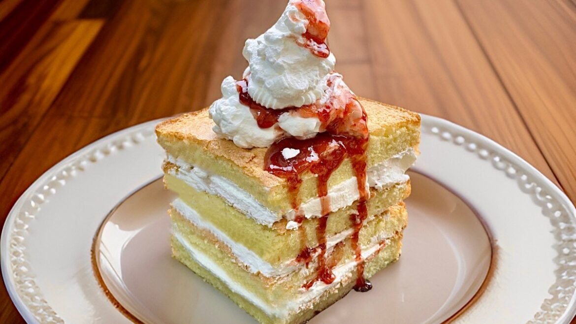 Three-layer vanilla cake with cream filling and strawberry sauce, topped with whipped cream on a plate