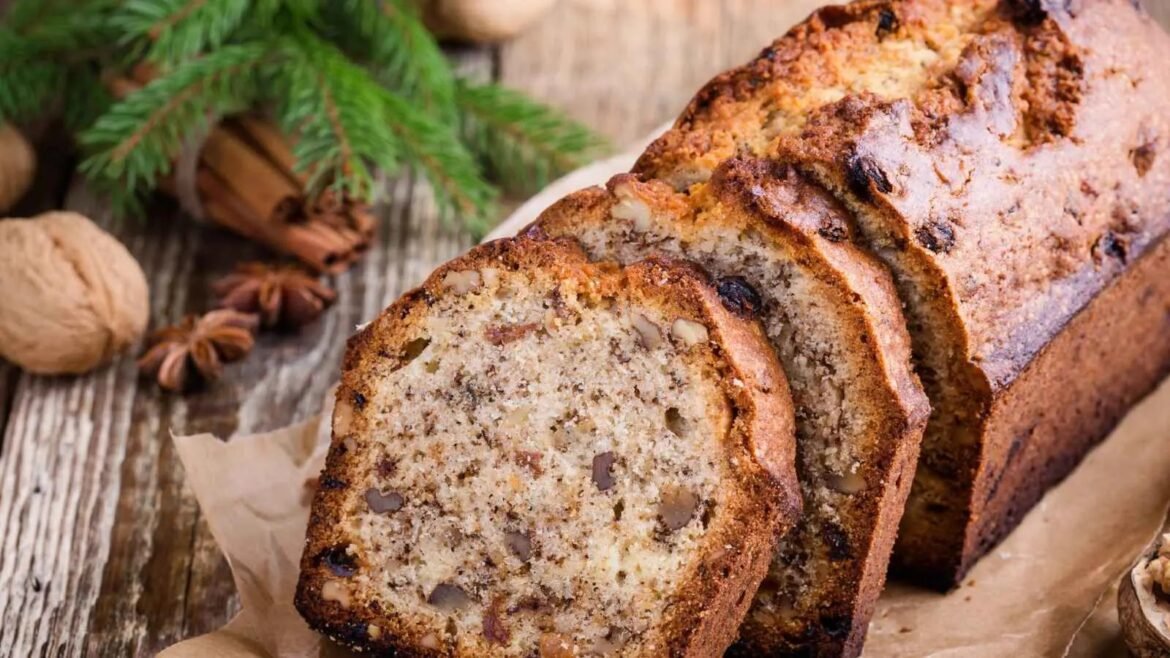 Sliced banana bread studded with walnuts on parchment, a rustic wooden surface and evergreen sprigs in the background.