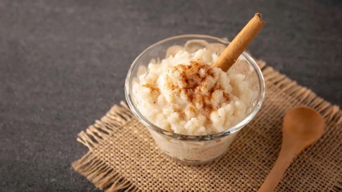 Rice pudding in a clear glass cup topped with cinnamon and a cinnamon stick on a burlap mat.