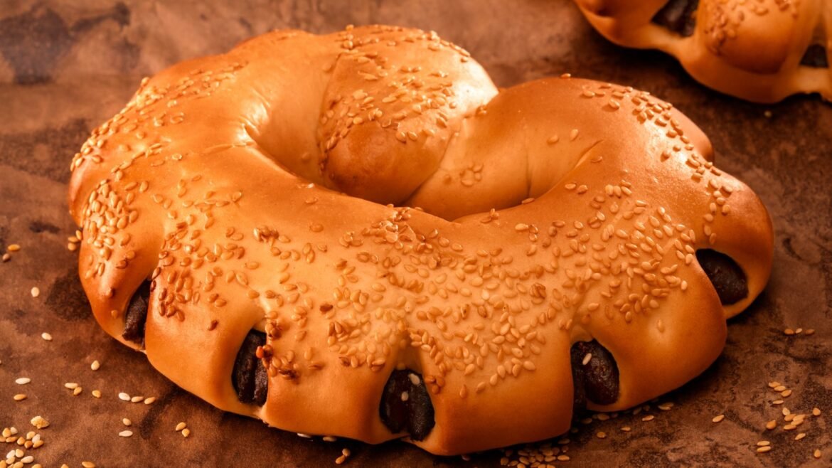 Sesame-topped bagel on a baking sheet, revealing the chewy ring shape and glossy crust.