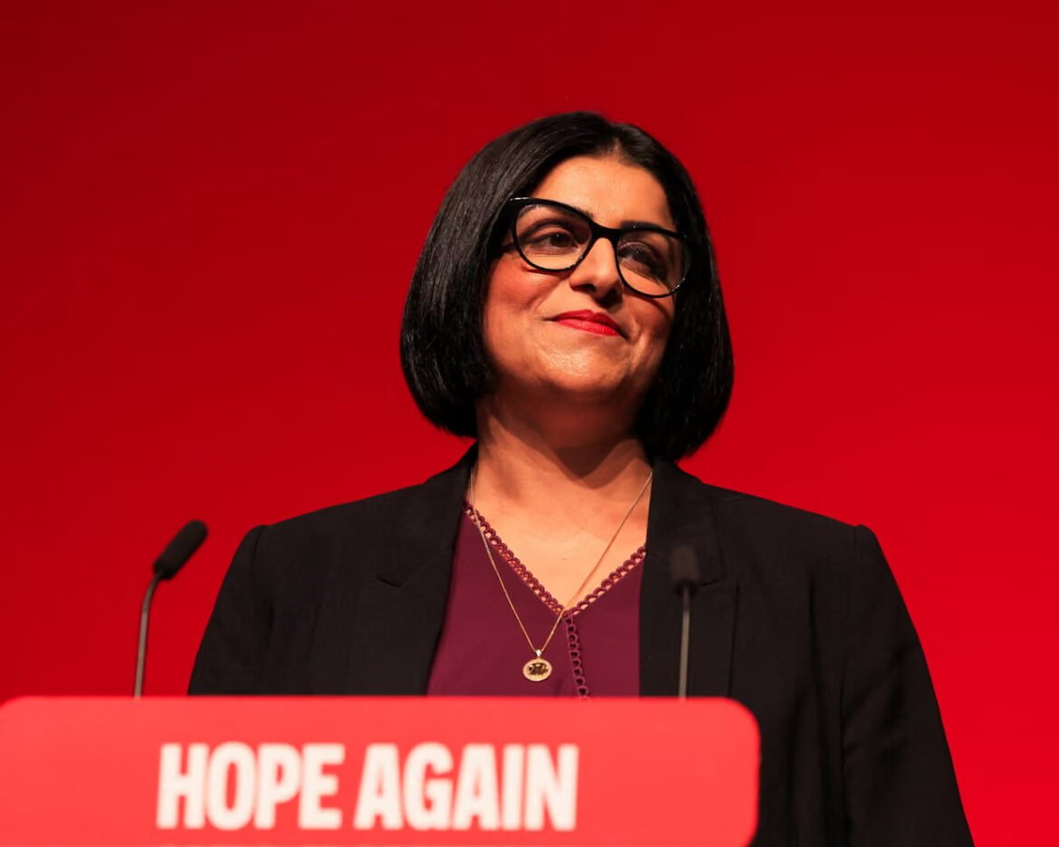Woman with black bob haircut and glasses speaking at a podium against a red backdrop, banner reads 'HOPE AGAIN' in white letters.
