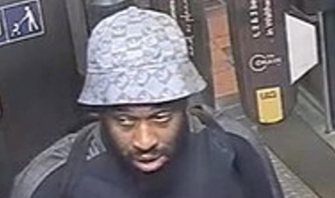 Man wearing a light patterned bucket hat, looking up inside a dim elevator or enclosed area.