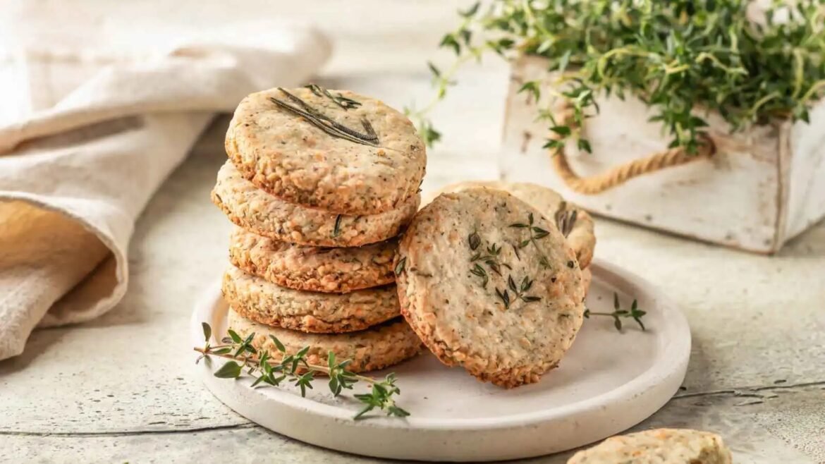 Stack of savory herb crackers with rosemary on a white plate, in a rustic setting.