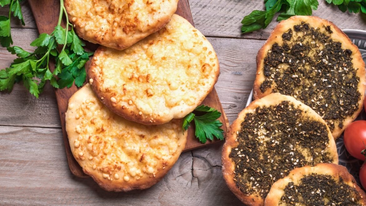 Assortment of cheesy and herb-topped flatbreads on a wooden board with parsley garnish and tomatoes nearby