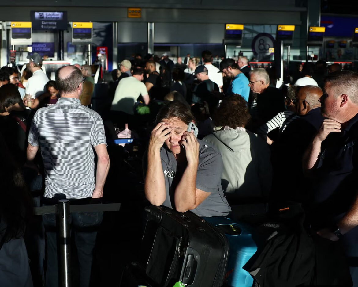 Man sitting with a large suitcase in a crowded airport terminal, holding a phone to his ear and touching his temples in apparent stress.