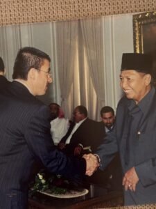 79390119828089640674028074238123518217424853n | Aleumumnews Two Men in Suits Shake Hands in a Formal Room with Seated Attendees Watching in the Background Aleumumnews