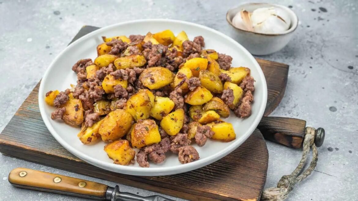 Crispy browned potato chunks sautéed with crumbled ground beef on a white plate atop a rustic wooden board.