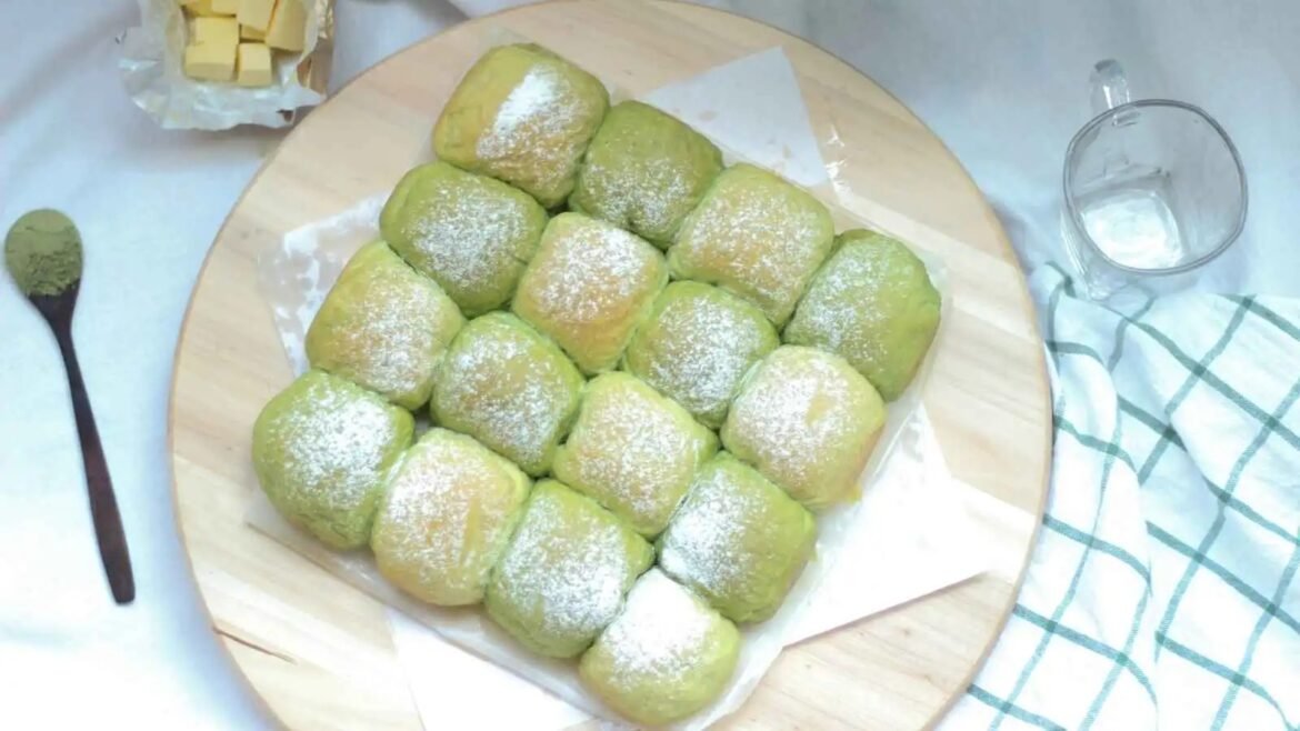 Pile of green square pastries dusted with powdered sugar on a round wooden board.