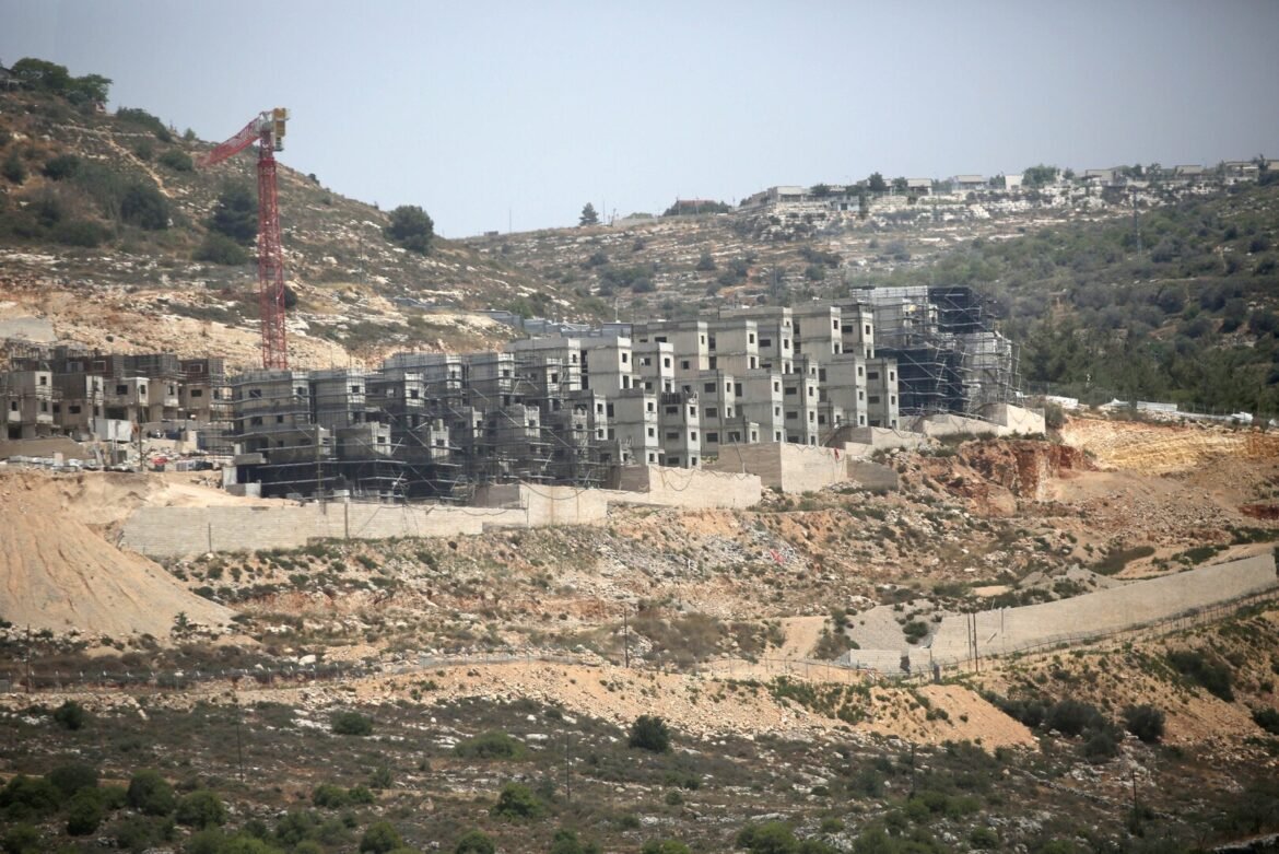 Row of grey unfinished apartment blocks on a hillside with extensive scaffolding and a red construction crane nearby.