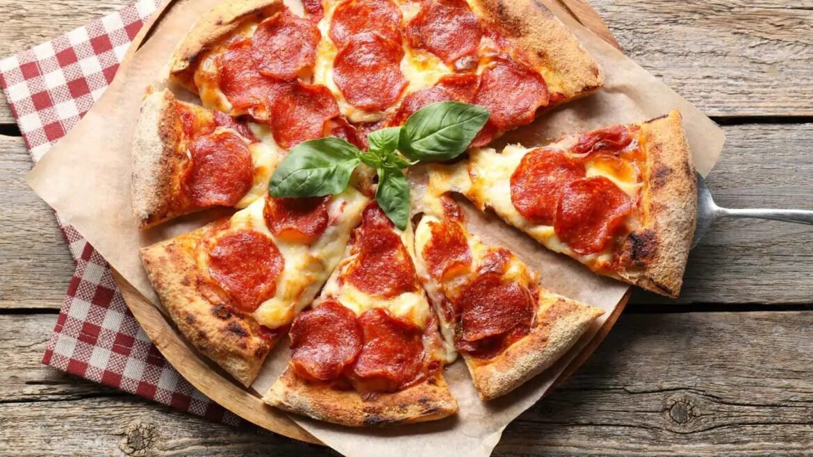 Pepperoni pizza on a wooden table, sliced and served on parchment with fresh basil garnish.