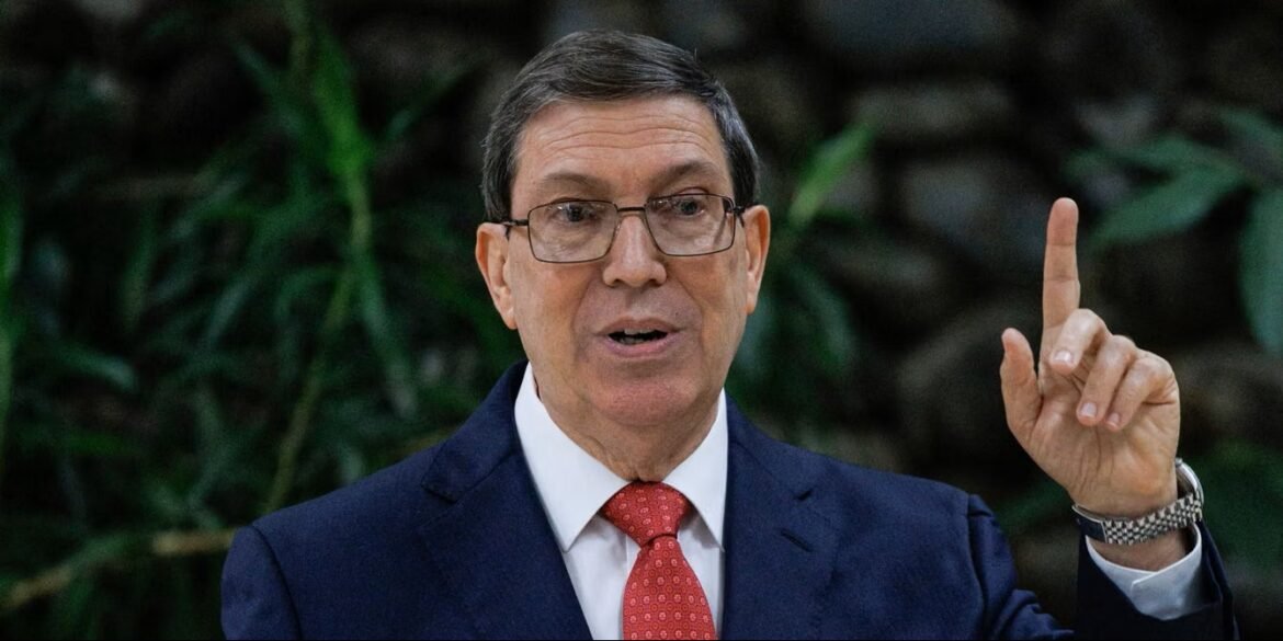 Man in a dark blue suit and red tie speaks, raising his right index finger as he gestures outdoors