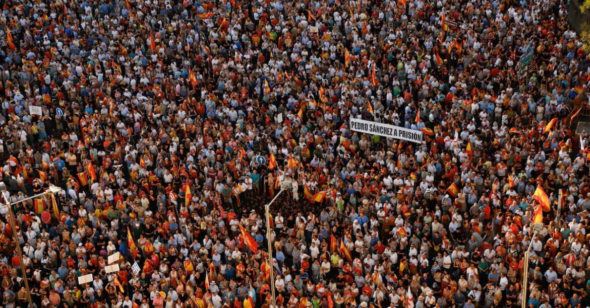 Massive crowd of protesters densely packed, many waving Spanish flags and a banner reading 'Pedro Sánchez a prisión'.