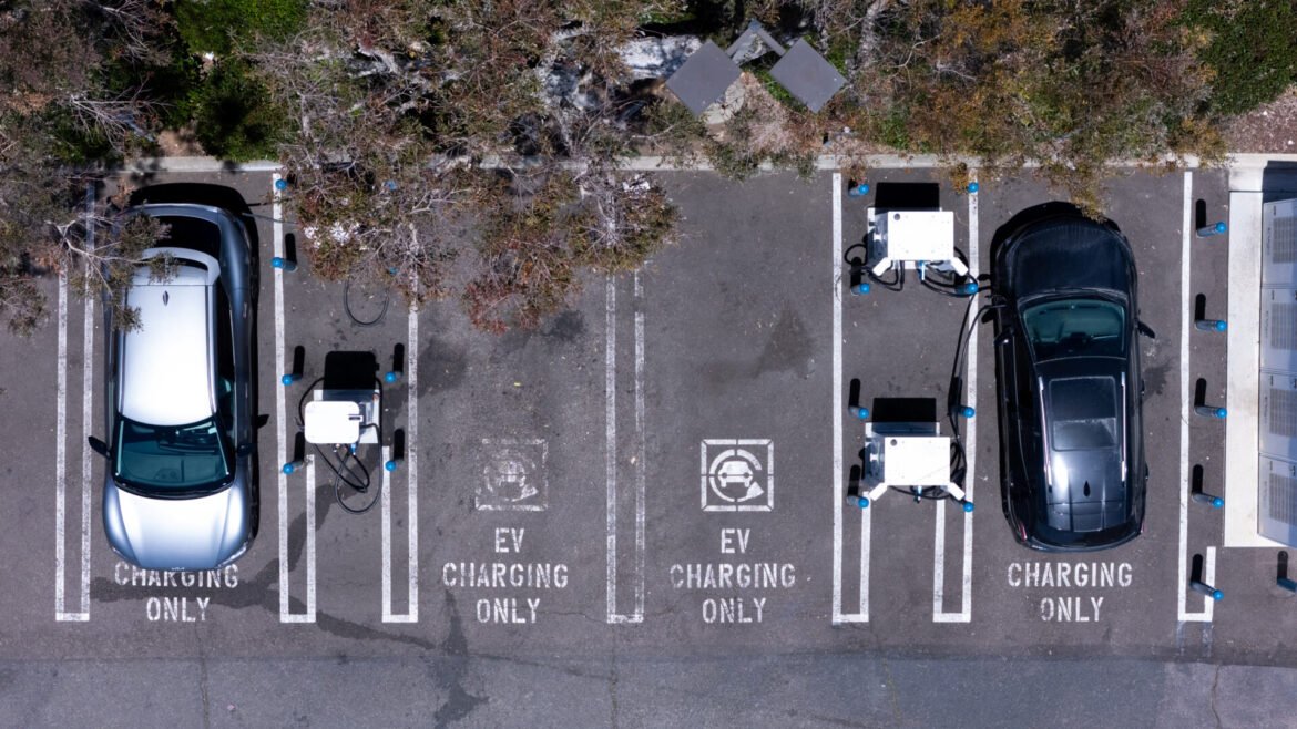 Aerial view of a parking lot with EV charging bays; cars are plugged in at several charging stations and marked EV CHARGING ONLY.