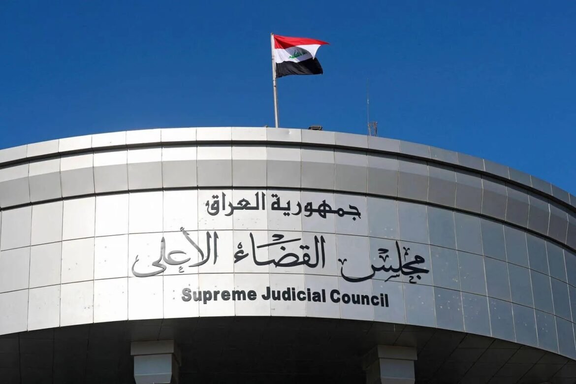 Flag of Iraq atop a curved government building with the Arabic and English sign: 'Supreme Judicial Council' on the facade.