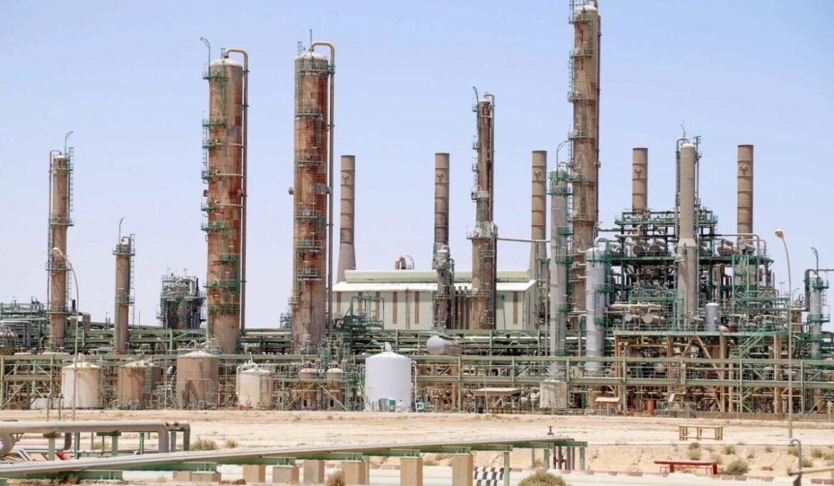 Large industrial refinery with multiple tall smokestacks and complex piping infrastructure against a clear sky.