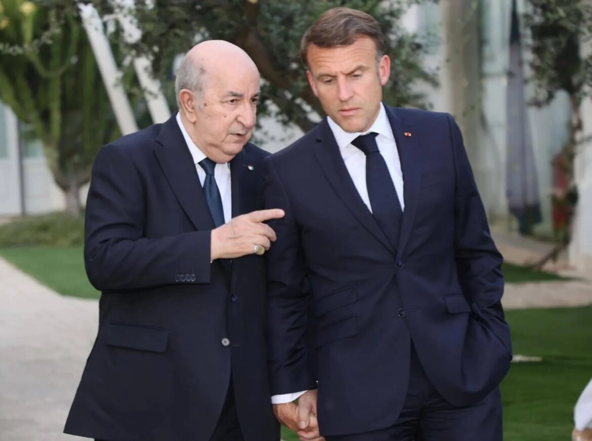 Two men in dark suits walk outdoors, one gesturing with his finger as they converse.