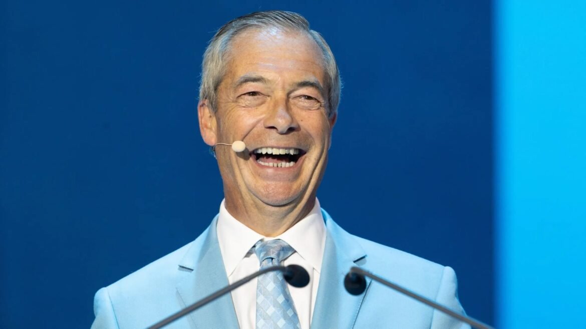 Smiling man with gray hair in a light blue suit and patterned tie giving a speech on stage with a microphone headset