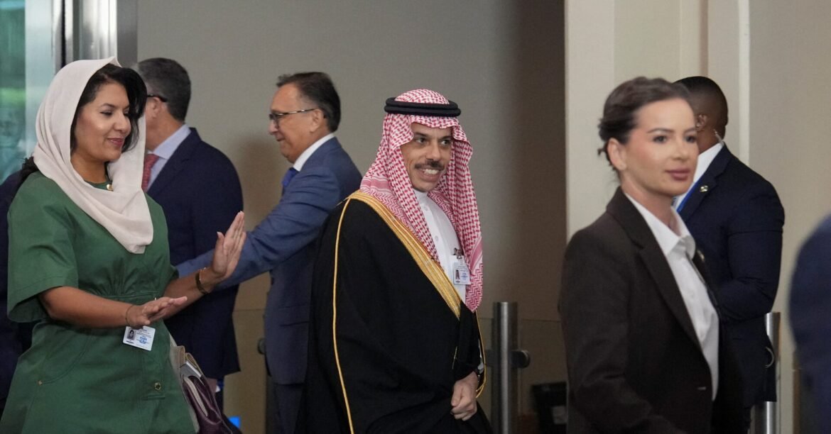 Smiling man in traditional Saudi attire walks with a group of professionals in a hallway.