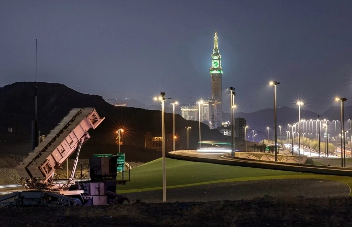 Nighttime highway scene with a tilted construction machine in the foreground and a tall illuminated clock-tower building in the distance.