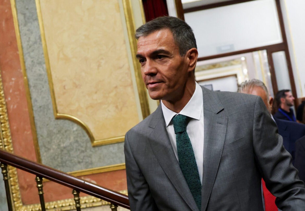 Man in a gray suit and teal tie walking down a marble staircase in an ornate interior.