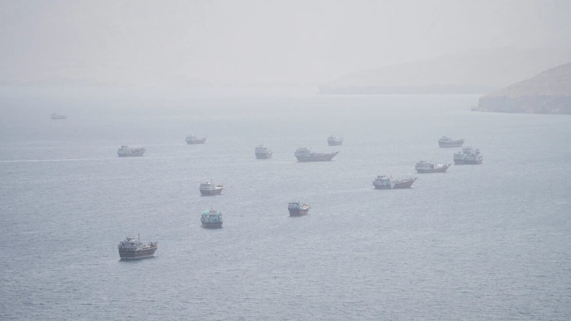 A misty sea scene with numerous small boats scattered across calm water and distant, hazy hills on the horizon