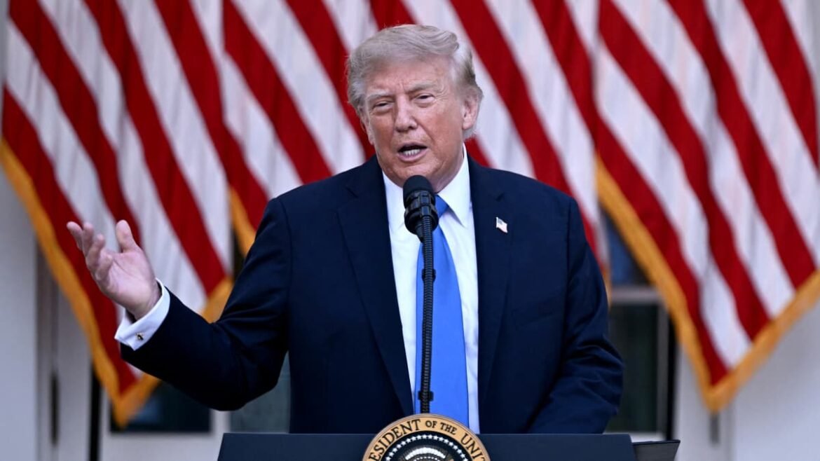 Man in a dark suit and blue tie speaks at a podium with the presidential seal, American flags in the background.