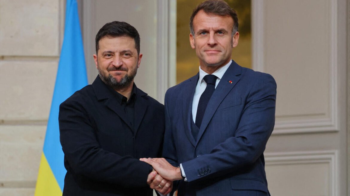 Two men in formal attire shake hands in front of a light-colored building, with a blue-and-yellow Ukrainian flag in the background.