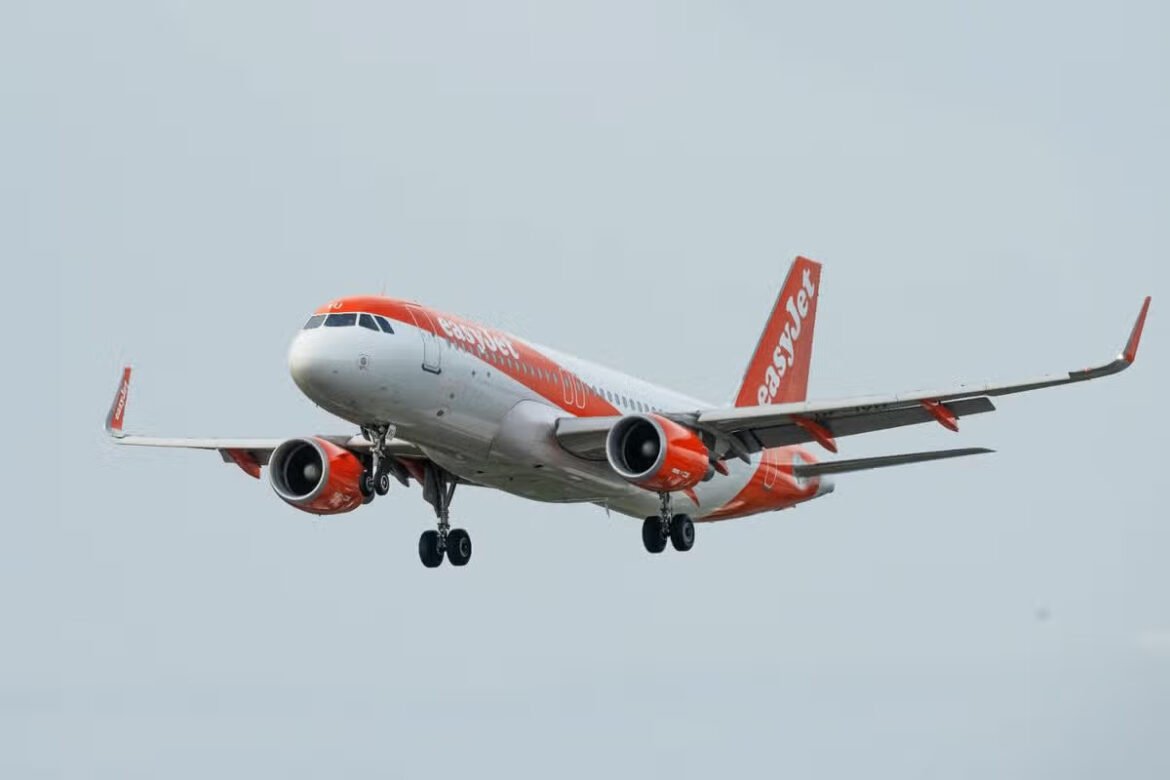 Orange-and-white EasyJet passenger jet in flight, landing gear down, angled from the front-left side.