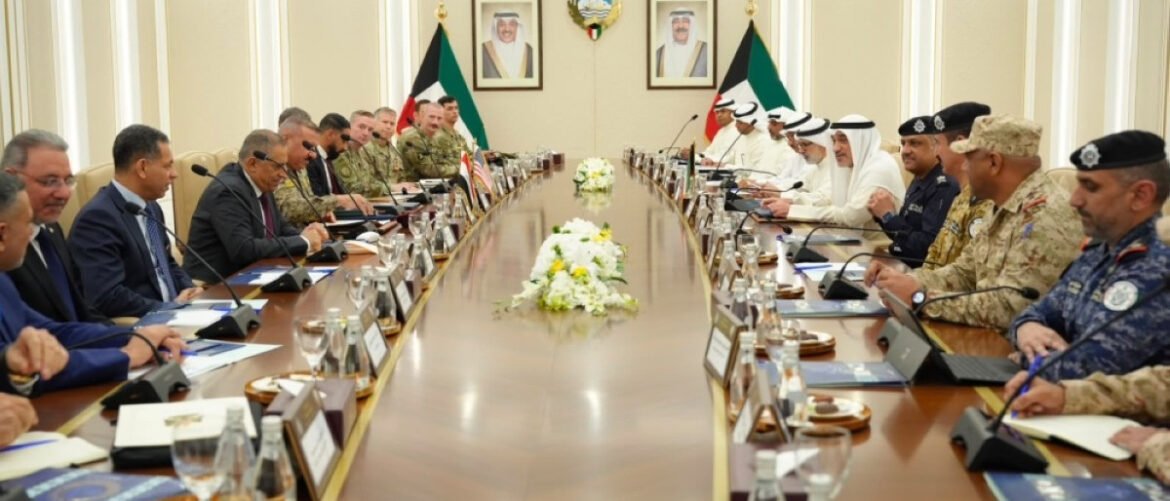 Leaders from multiple nations sit on both sides of a long conference table in a formal meeting room, with flags and portraits on the wall behind.