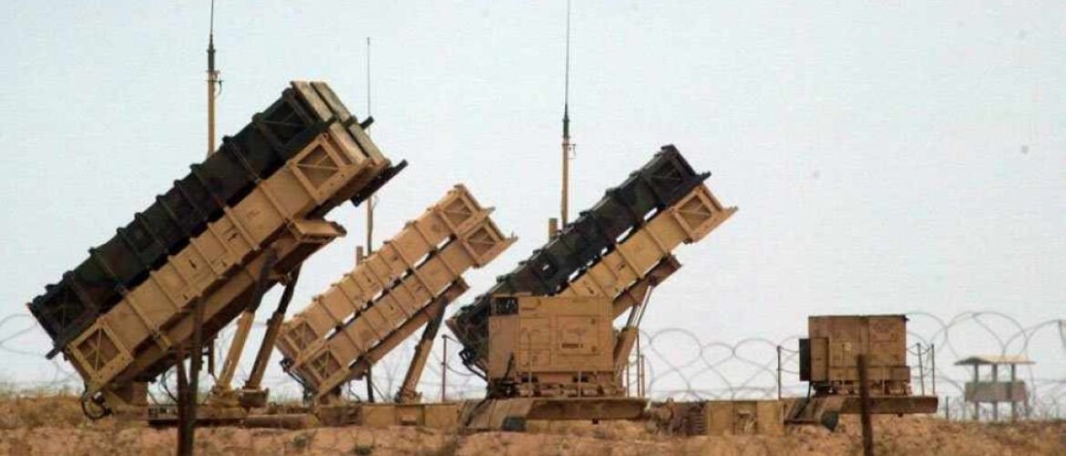 Desert military launchers angled skyward on wheeled platforms with a barbed-wire fence in the foreground.