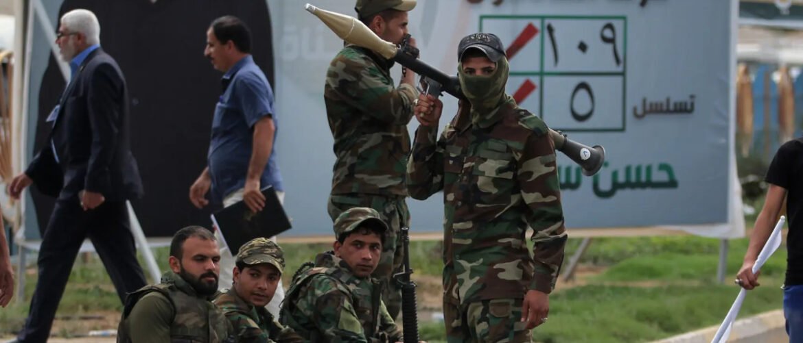 Camouflaged soldiers posing with a rocket launcher outdoors, with a banner in the background.