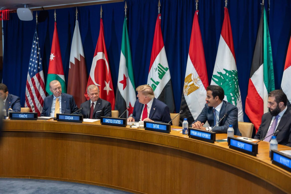 Prestigious international meeting with world leaders seated at a curved wooden table, flags from many nations behind them, and nameplates in front of each delegate.