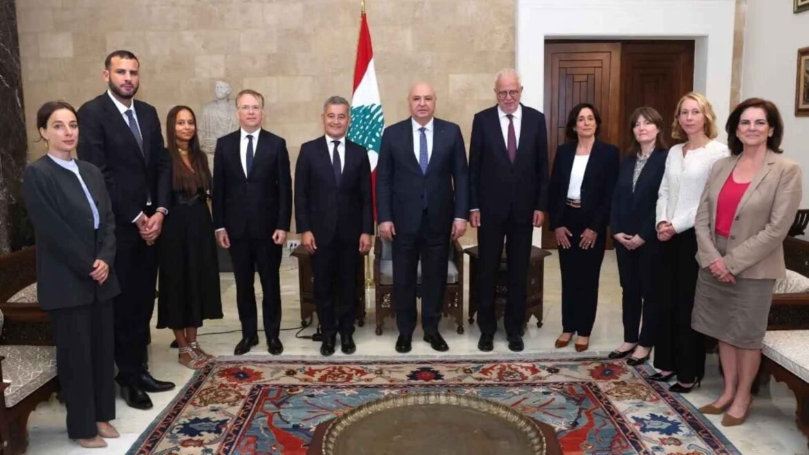 Group of formally dressed officials posing for a photo in a government room with a flag in the background.