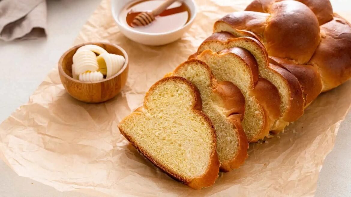 Loaf of sliced golden bread on parchment with butter curls and honey nearby on a rustic table