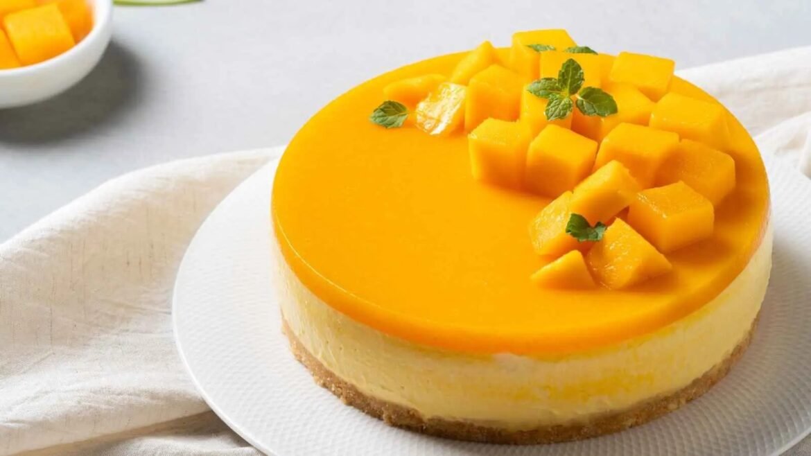 Mango cheesecake with an orange mango glaze, topped with mango cubes and a few mint leaves on a white plate.