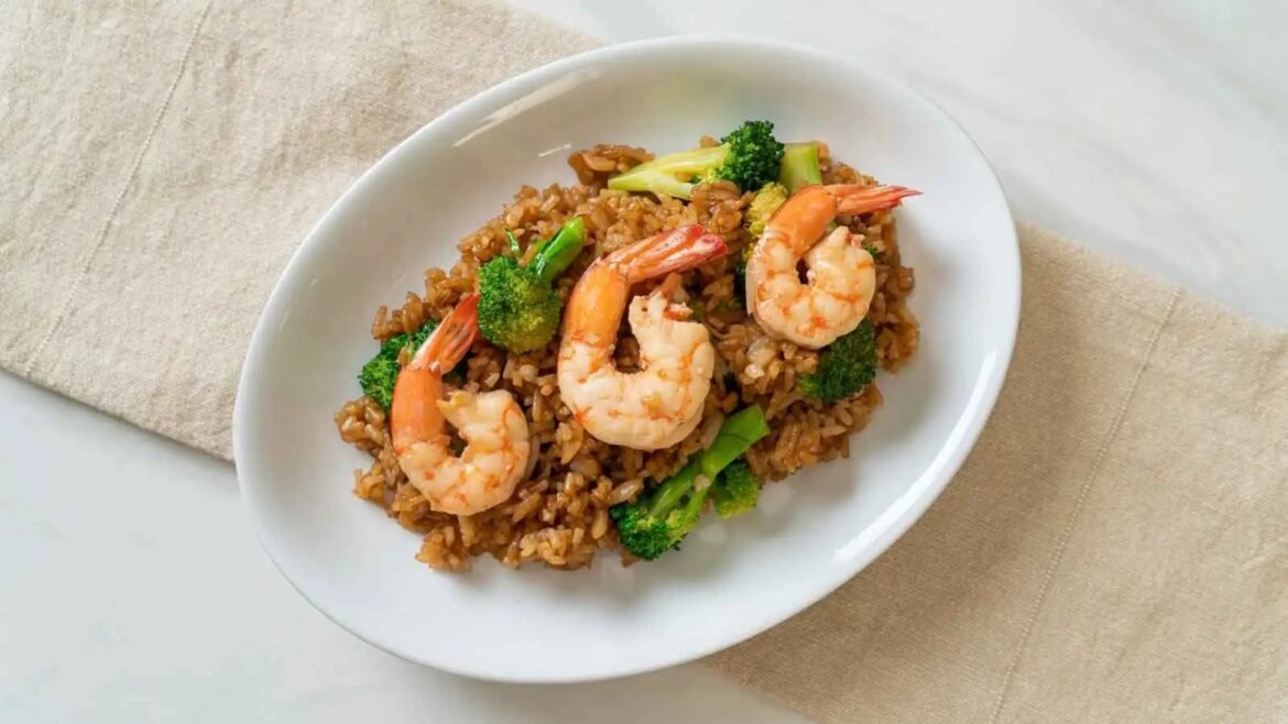 Plate of fried rice with shrimp and broccoli on a white oval dish on a light tablecloth