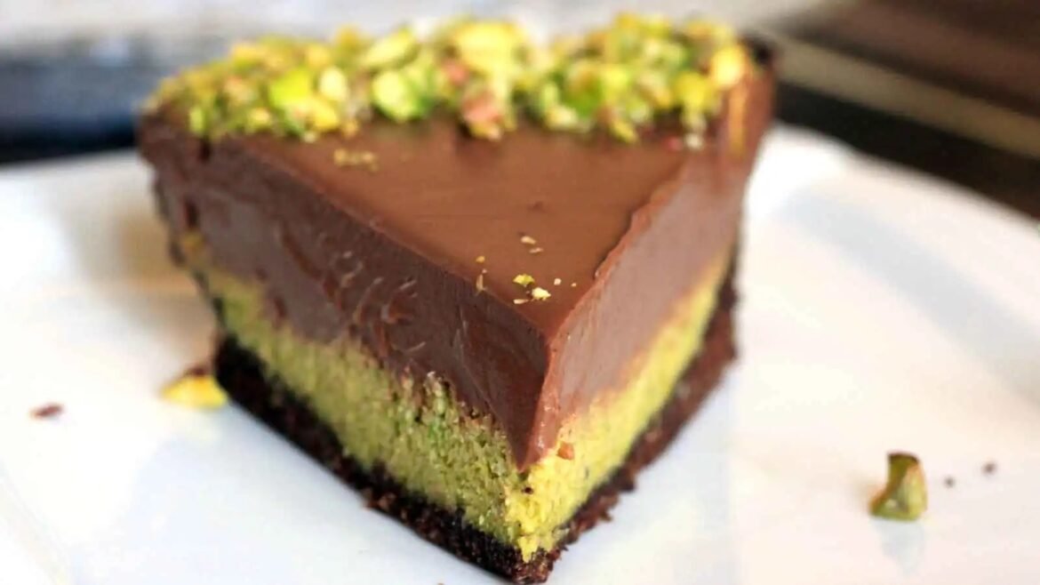 Tri-layer chocolate-pistachio dessert slice with a pistachio topping on a white plate