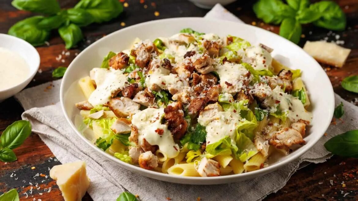 Bowl of pasta with grilled chicken, chopped greens, and a creamy white cheese sauce topped with parmesan shavings.