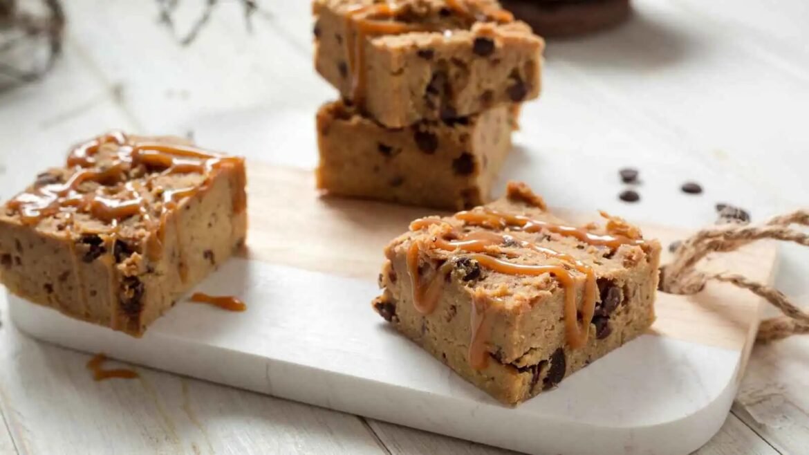 Squares of caramel-drizzled chocolate chip cookie bars on a wooden board