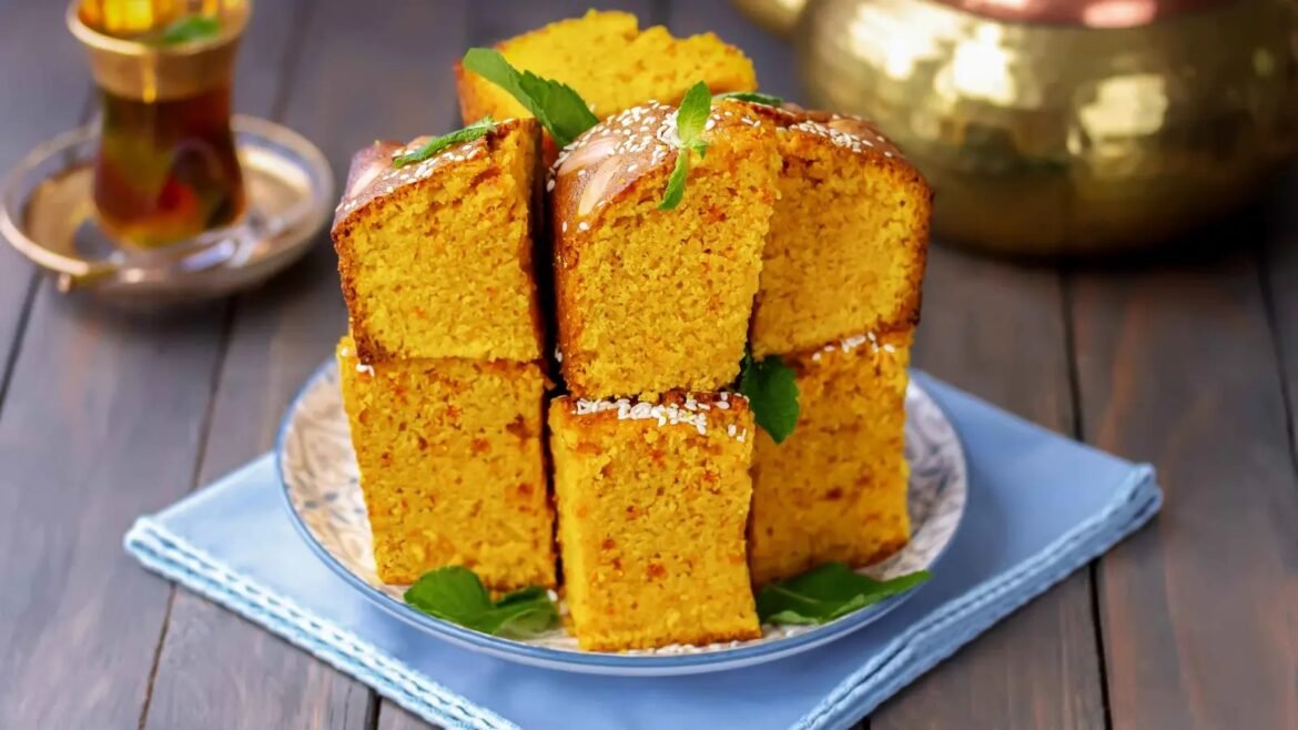 Stack of orange sponge cake cubes stacked on a plate, topped with sesame seeds and mint leaves.